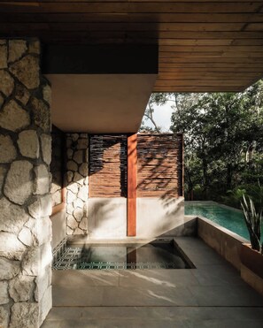 A modern outdoor pool area with stone walls, a wooden ceiling, and a clear view of the surrounding greenery. - Siwa Jungle Romance C1-002 Beach Club Access (Tulum)