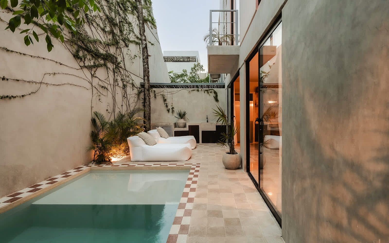 Un espace piscine extérieur moderne, avec un sol à carreaux, des chaises longues blanches et des plantes en pot.