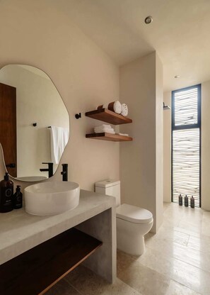 Ein modernes Badezimmer mit einem großen Spiegel, einem weißen Waschbecken, einer Toilette und Holzregalen darüber.