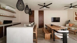 Eine moderne Küche mit Kochinsel, Holzbänken, Pendelleuchten, Deckenventilatoren und einem Flachbildfernseher an der Wand.
