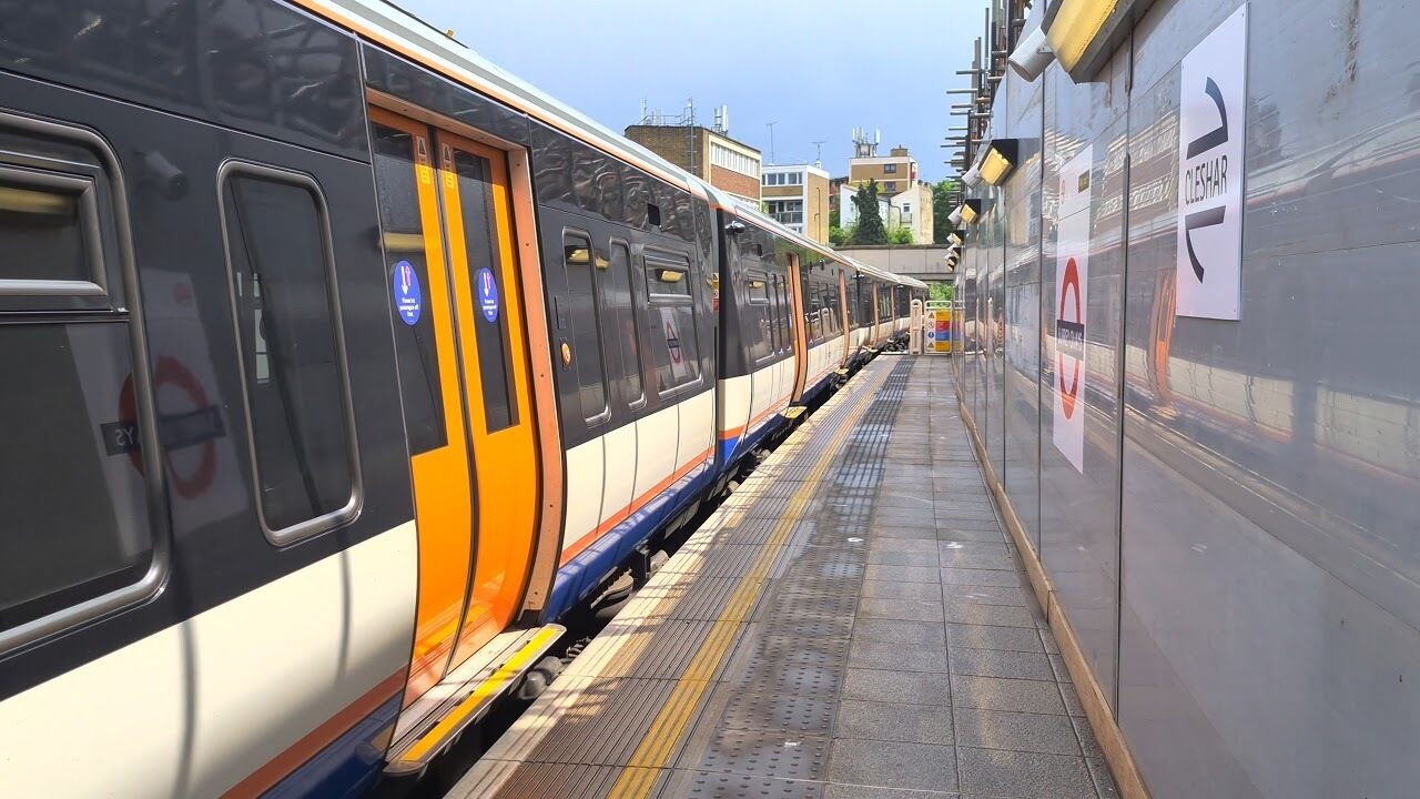 Un andén de estación de tren, con un tren a la izquierda y un cartel de la estación a la derecha.