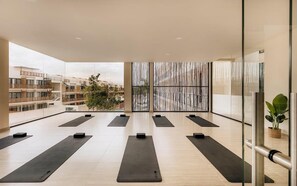 Un vaste espace intérieur aménagé avec de nombreux tapis de yoga disposés en rangées, de grandes fenêtres et une vue sur les bâtiments environnants.