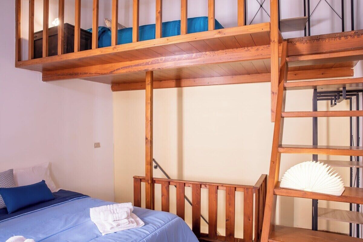 Een slaapkamer met een stapelbed, een houten trap en een plank met een ventilator.