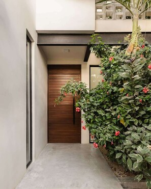 A modern building with a wooden door, a concrete pathway, and a large plant with red flowers. - Villa Anunna Luxe Tulum Villa Beach Club Access (Tulum)