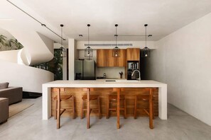 A modern kitchen with a central island, wooden bar stools, pendant lighting, and a built-in refrigerator. - Villa Anunna Luxe Tulum Villa Beach Club Access (Tulum)
