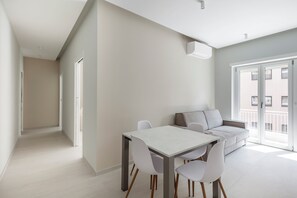 Ein modernes, minimalistisches Wohnzimmer mit Essbereich, ausgestattet mit einer Couch, einem Esstisch und einem großen Fenster mit Blick auf die Stadt.