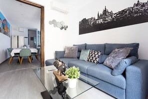 A modern living room with a blue sofa, a glass coffee table, and a cityscape wall art. - DownTown La Latina Grupos, by MoNARO (Madrid)