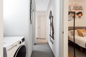 A hallway leading to a bedroom with a bed, a washing machine, and a wall with a mural. - DownTown La Latina Grupos, by MoNARO (Madrid)