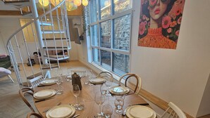 A dining area with a wooden table set for six, surrounded by white chairs.
