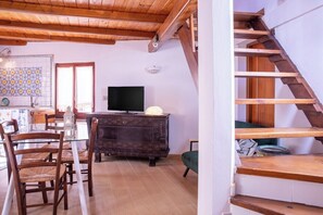 A room with a wooden ceiling, a TV on a dark wooden cabinet, a dining table with chairs, and a staircase. - La Cambusa Apartment 2 (Alghero)