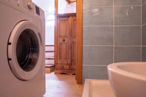 A laundry area with a washing machine, wooden cabinet, and tiled walls. - La Cambusa Apartment 2 (Alghero)