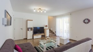 Un saló modern amb un sofà, una taula de centre de vidre, un televisor de pantalla plana, una escala i un rellotge a la paret.