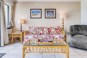 A living room with a sofa, two side tables, a coffee table, and a grey armchair. - Maui Kamaole #H-105 Ocean View Condo across the street from beach A/C (Kihei)