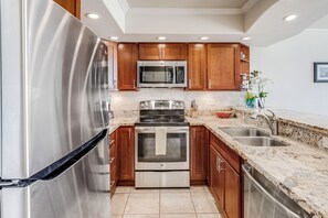 A modern kitchen with stainless steel appliances, wooden cabinets, granite countertops, and a built-in oven. - Maui Kamaole #H-105 Ocean View Condo across the street from beach A/C (Kihei)