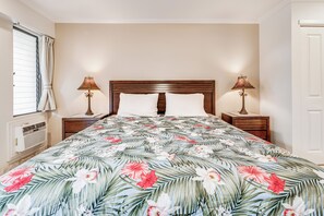 A bedroom with a floral bedspread, two bedside lamps, and a window with curtains. - Maui Kamaole #H-105 Ocean View Condo across the street from beach A/C (Kihei)