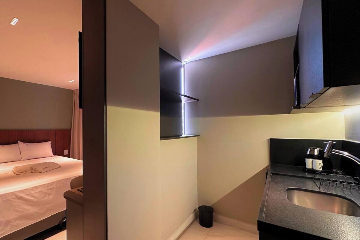 A modern hotel room with a neatly made bed, a small bedside table, and a built-in sink with a mirror.