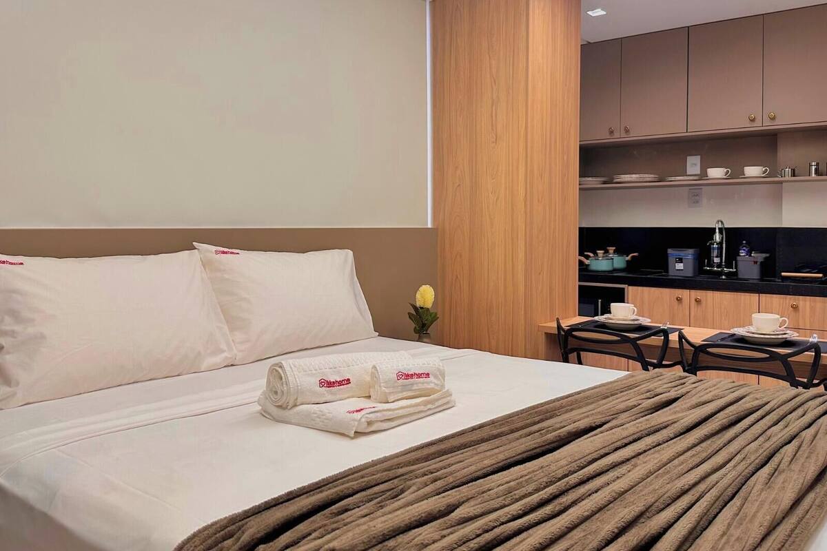 A hotel room with a bed, a small table with chairs, a kitchenette, and a vase with flowers.