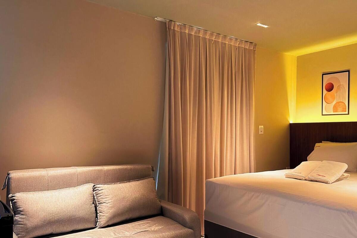 A hotel room with a bed, a sofa, and a large window with curtains.