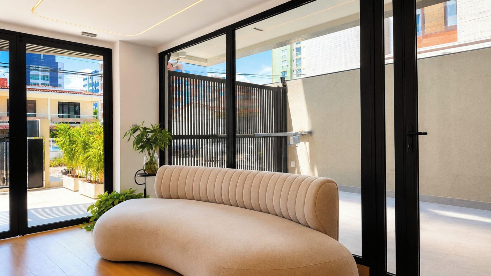 Uma sala de estar moderna com um sofá curvo, grandes janelas e vista para a paisagem urbana.