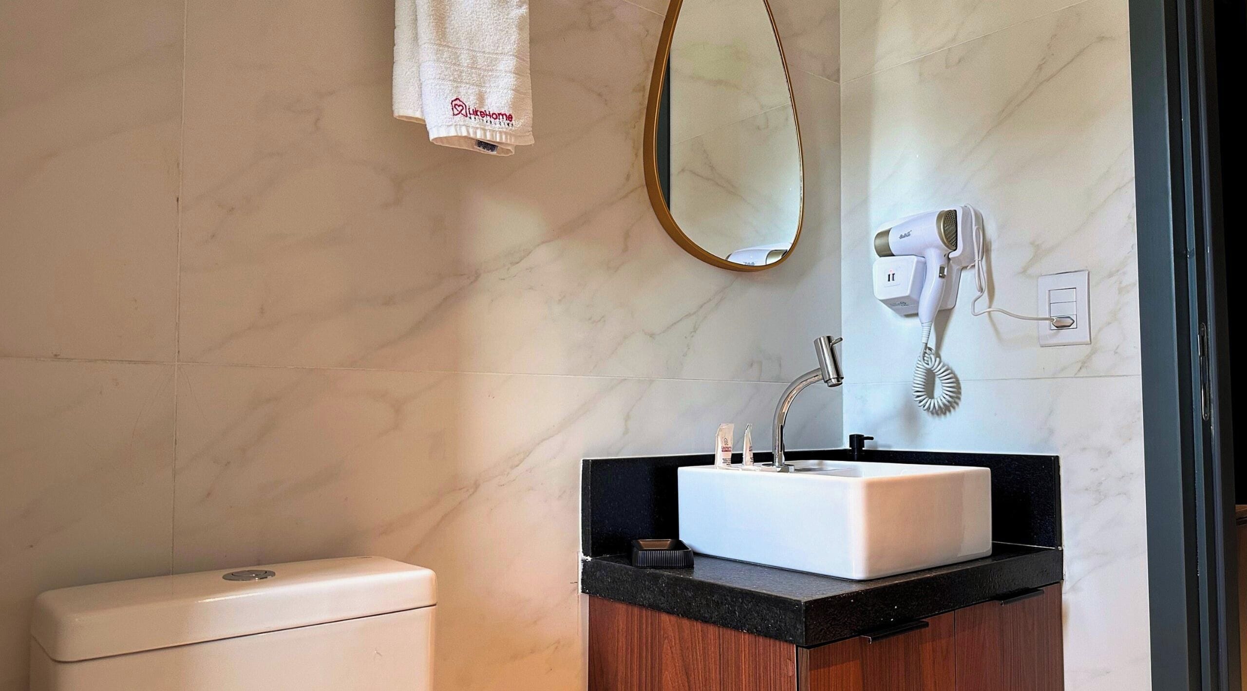 A bathroom with a white toilet, a sink with a black countertop, a mirror, and a hairdryer mounted on the wall.