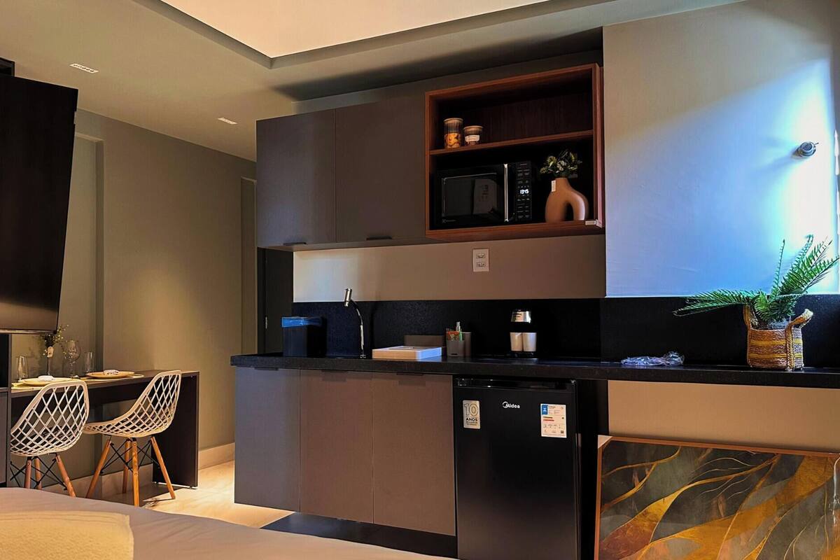 A compact kitchen with a microwave, coffee maker, and a small refrigerator. There is a dining area with a chair and a table.