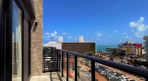 Ein Balkon mit Blick auf einen Parkplatz, Gebäude und das Meer.