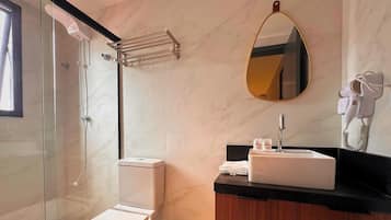 Uma casa de banho moderna com cabine de duche em vidro, sanita, lavatório com espelho e secador de cabelo fixado na parede.