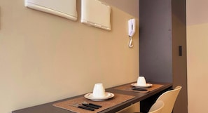 Une chambre d’hôtel avec une table à manger dressée pour deux personnes, un téléphone fixé au mur et un appareil de climatisation.