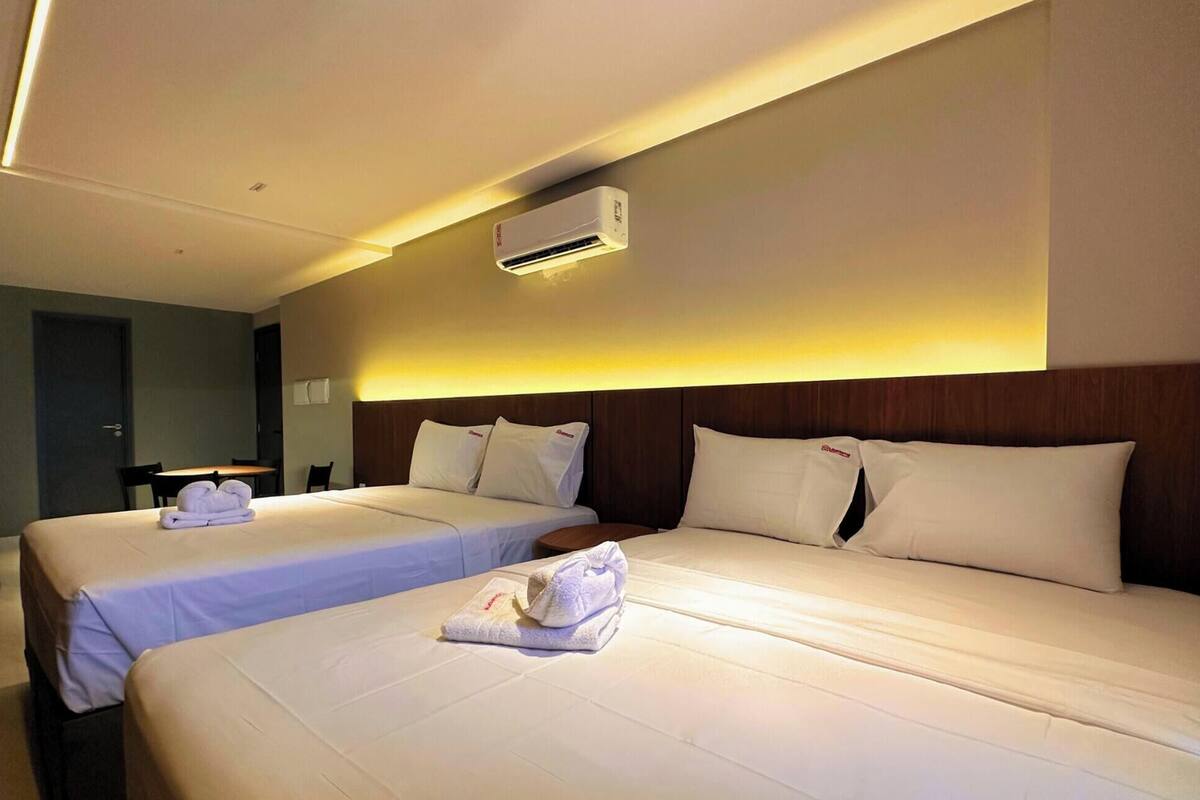 A hotel room with two beds, a bedside table, an air conditioning unit, and a curtain.