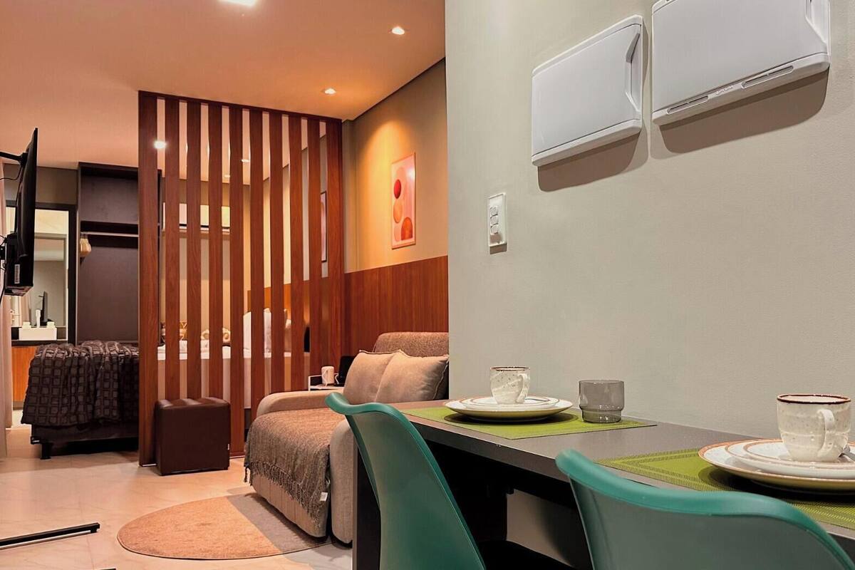 A modern hotel room with a dining area, a sofa, a small table, and an air conditioning unit.