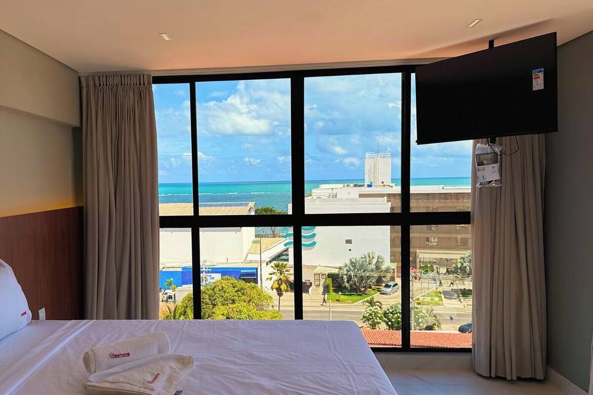 A hotel room with a large bed, a flat-screen TV, and a view of the ocean and cityscape.