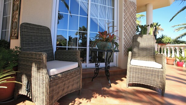 A patio with wicker chairs and a table, surrounded by potted plants and a large window. - 4 Bedroom Villa Sleeps 8 With Private Pool (Vera)