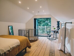 A bedroom with a large bed, a balcony with a view of greenery, and a camera on a tripod. - Bydown Barn in Swimbridge (Barnstaple)