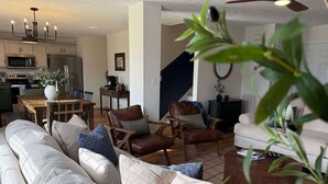 Een woonkamer met een bank, twee leren fauteuils, een salontafel en een eethoek met een tafel en stoelen.