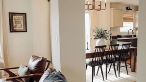 Een moderne woonkamer met een bank, een eethoek met stoelen en een tafel, en een keuken op de achtergrond.