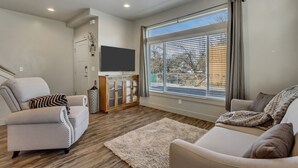 A modern living room with a flat-screen TV, two sofas, a wooden cabinet, and a large window with blinds. - Hill Field 2 and 3 by CDH Double Town Homes (Layton)