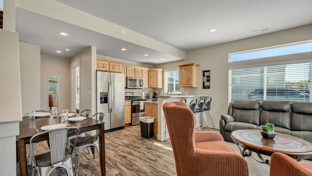 A modern kitchen with wooden cabinets, stainless steel appliances, and a dining area with metal chairs. - Hill Field 2 and 3 by CDH Double Town Homes (Layton)