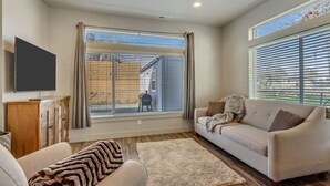 A living room with a sofa, a TV, and a large window with blinds. - Hill Field 2 and 3 by CDH Double Town Homes (Layton)