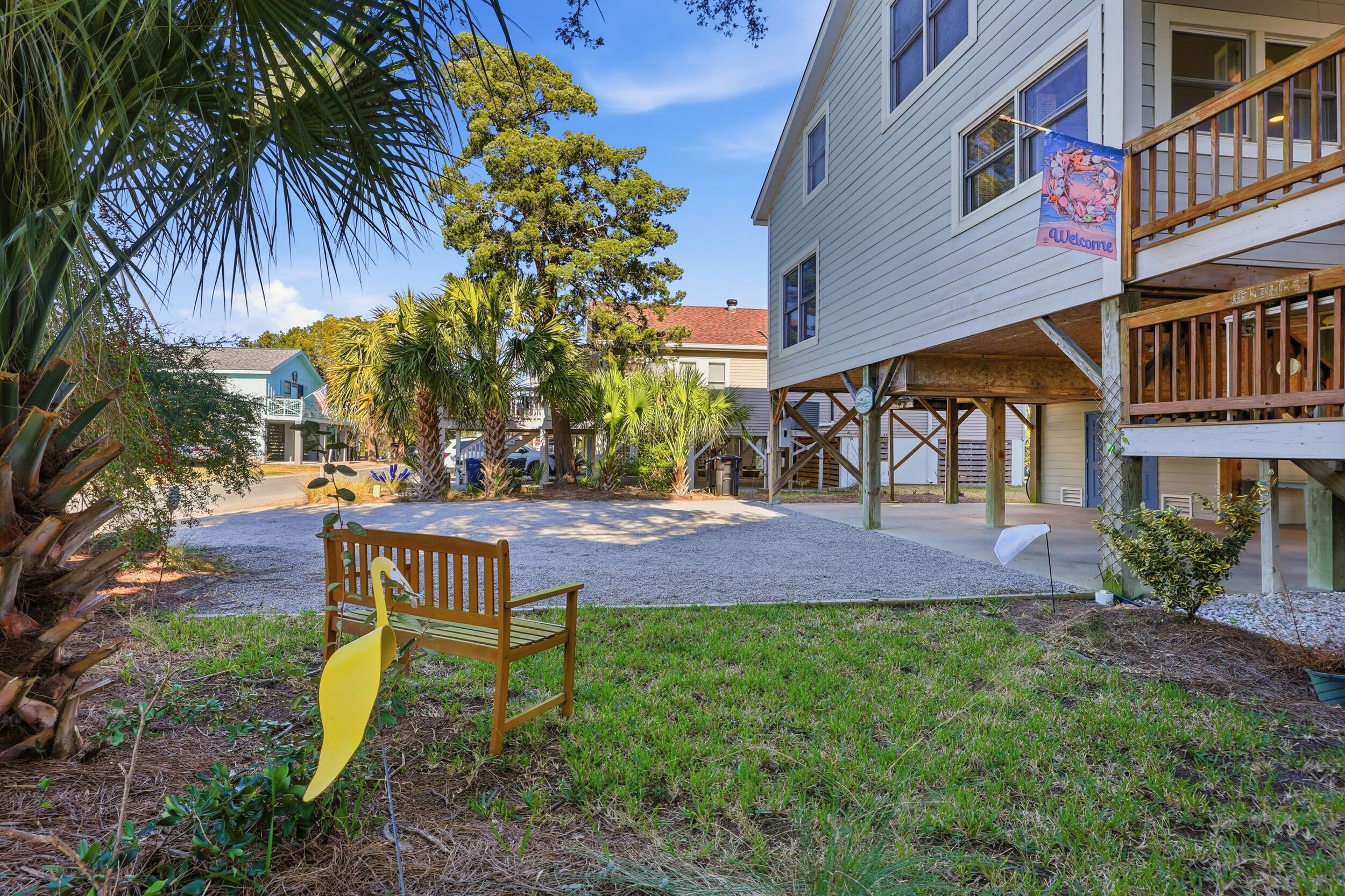 A building with a 'Welcome' sign, a wooden bench, and a palm tree in the foreground.