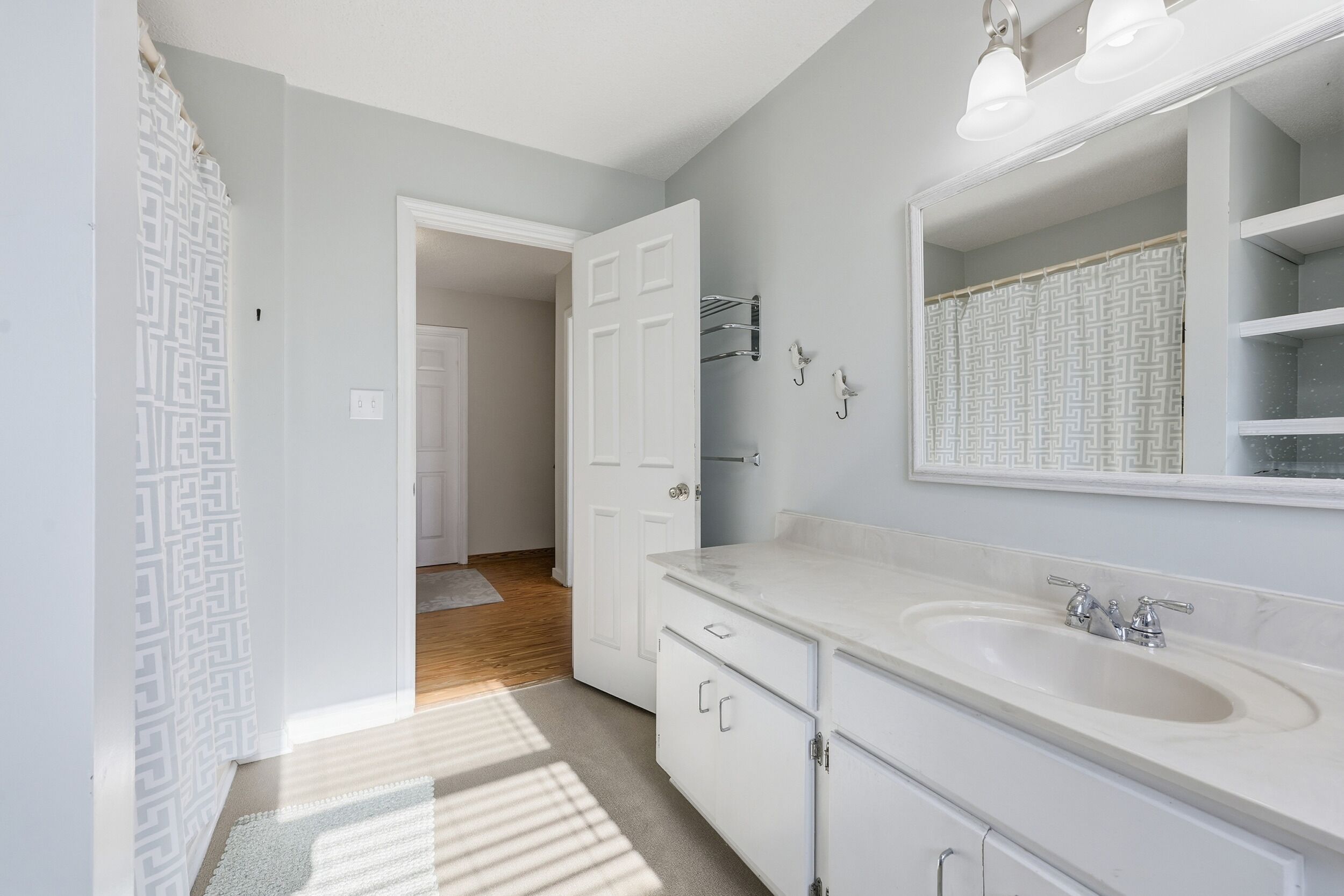 Une salle de bain avec un meuble-lavabo blanc, un grand miroir et un espace douche.