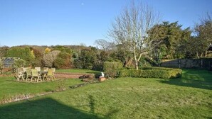 Un giardino curato con prato, un patio con sedie e diverse piante e arbusti.