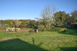 A well-maintained garden with a lawn, a patio with chairs, and a variety of trees and shrubs. - Country House near Deal & Sandwich (Tilmanstone)