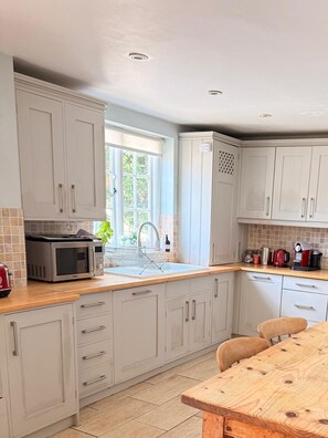 A kitchen with white cabinets, a wooden countertop, a stainless steel microwave, and a wooden dining table. - Country House near Deal & Sandwich (Tilmanstone)