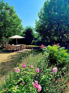 Un jardí amb taula i cadires sota una tanca, envoltat de flors i arbres en flor.