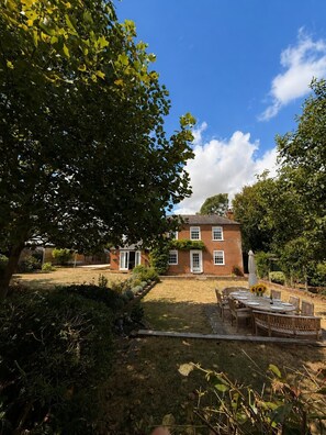 Ein zweistöckiges Backsteinhhaus mit Gartenpati und Außenmöbeln.