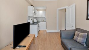 Un espacio habitable compacto con kitchenette, un televisor de pantalla plana, un sofá y una puerta que da a otra habitación.