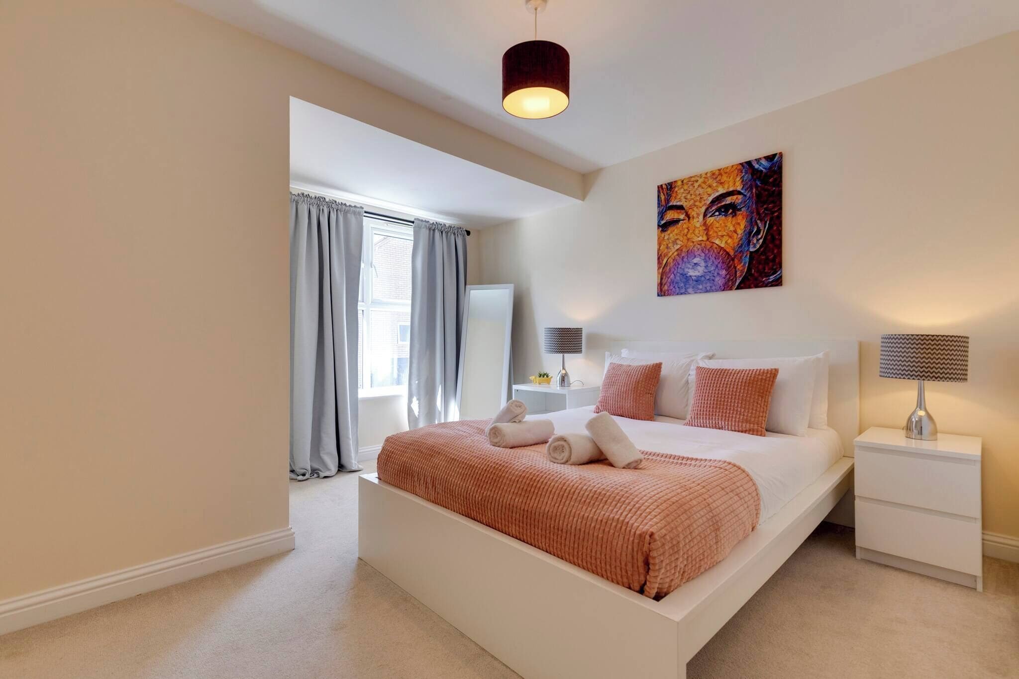 A modern bedroom with a large bed, a bedside table, a lamp, and a painting on the wall.