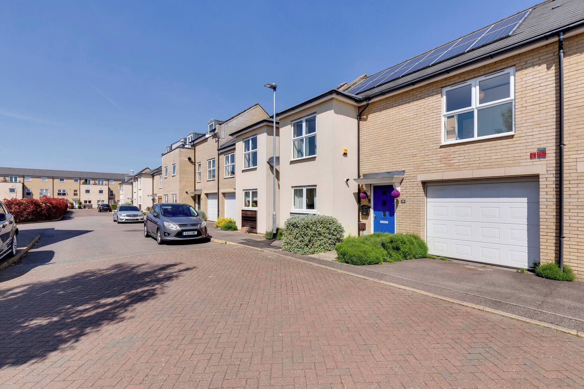A residential street with terraced houses, each with a garage and a small front garden.