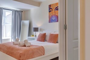 Een slaapkamer met een bed, kussens, een nachtkastje, een lamp en een schilderij aan de muur.