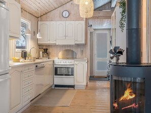 A kitchen with white cabinets, a stove, a clock, and a wood-burning stove. - "Irma" - 300m from the sea by Interhome (Hadsund)